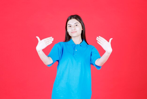 Ragazza in camicia blu in piedi su sfondo rosso e che indica se stessa