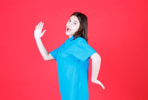 Ragazza in camicia blu in piedi sul muro rosso e scappando.