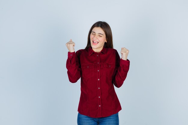 ragazza in camicia bordeaux che mostra il gesto del vincitore e sembra felice