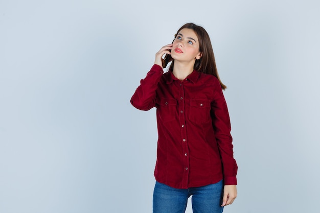 ragazza in camicia bordeaux che parla su smartphone e sembra pensierosa