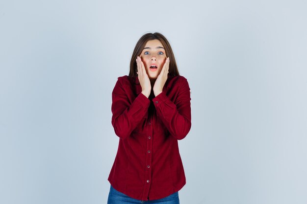 ragazza in camicia casual che tiene le mani vicino al viso e sembra sorpresa