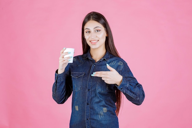 Ragazza in camicia di jeans che gode di una tazza di caffè usa e getta