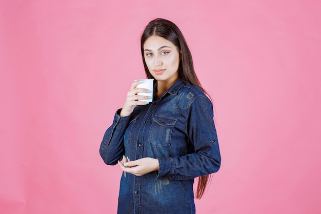 Ragazza in camicia di jeans che gode di una tazza di caffè usa e getta