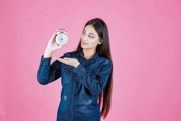 Ragazza in camicia di jeans che tiene e promuove una sveglia