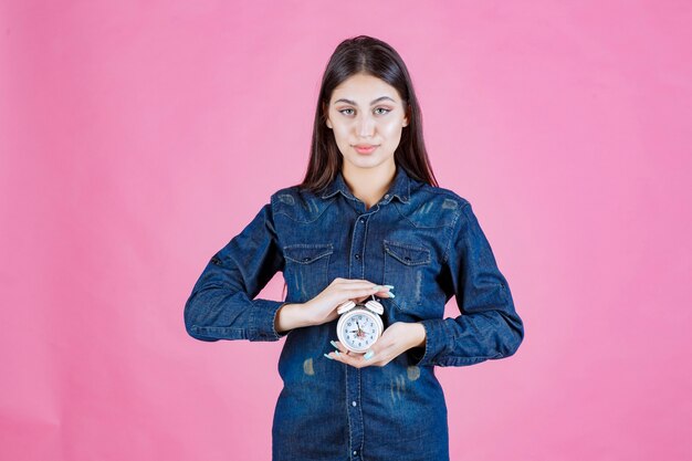 Ragazza in camicia di jeans che tiene la sveglia tra le mani