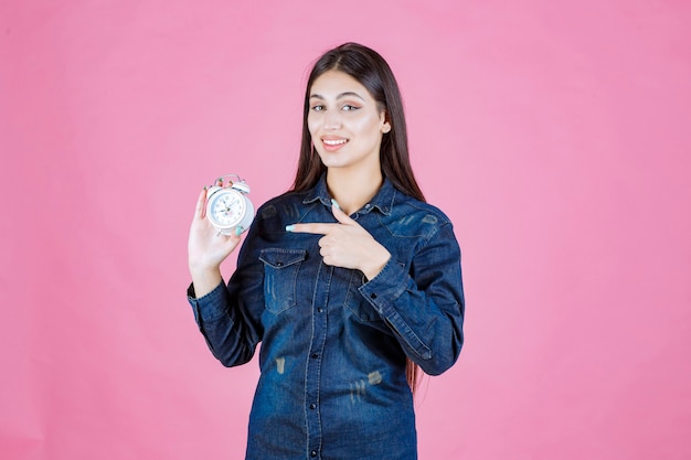 Ragazza in camicia di jeans tenendo la sveglia e indicandola