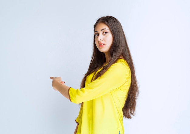 Ragazza in camicia gialla che indica da qualche parte.