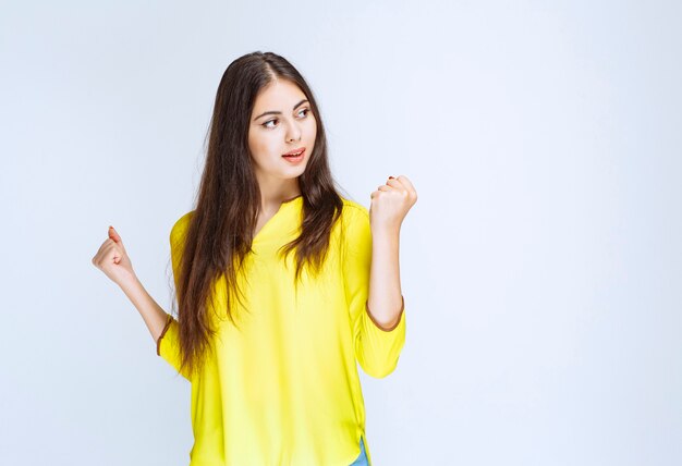 Ragazza in camicia gialla che mostra il pugno in segno di successo.