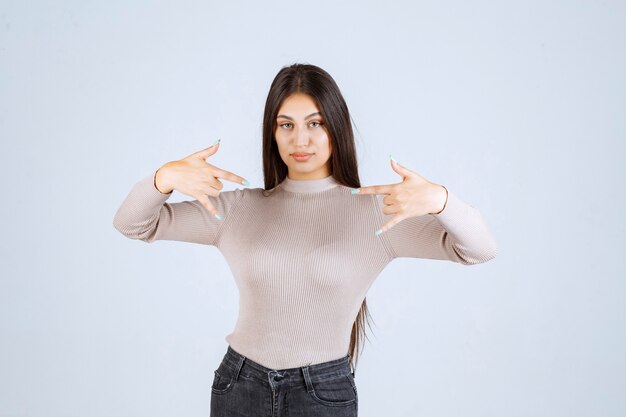 Ragazza in camicia grigia che fa il segnale di chiamata.