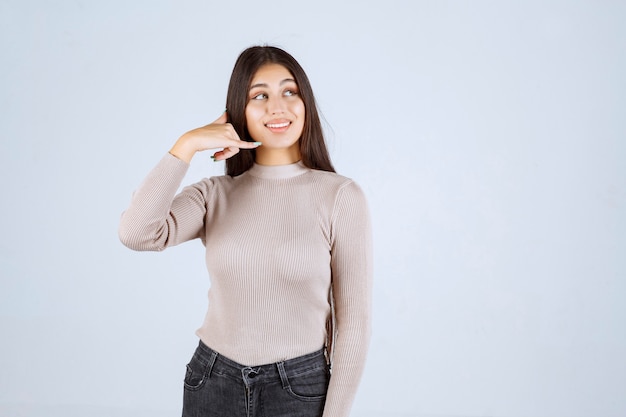 Ragazza in camicia grigia che fa il segnale di chiamata.