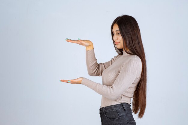 Ragazza in camicia grigia che mostra l'altezza di un oggetto.