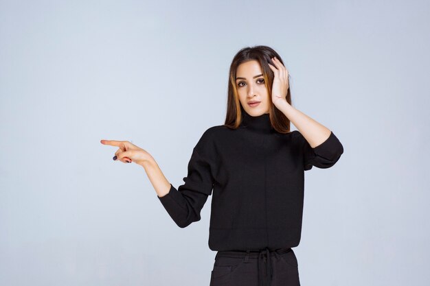 Ragazza in camicia nera che indica qualcosa a sinistra. Foto di alta qualità