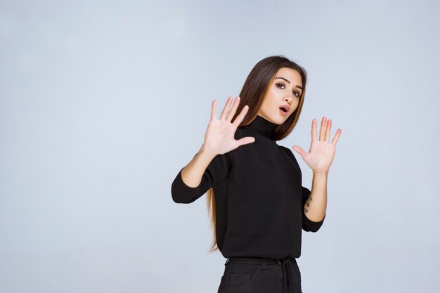 Ragazza in camicia nera che si ferma e impedisce qualcosa. Foto di alta qualità