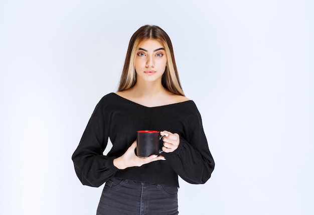 Ragazza in camicia nera che tiene una tazza di caffè nero. Foto di alta qualità