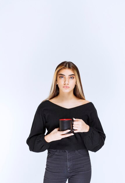 Ragazza in camicia nera che tiene una tazza di caffè nero. Foto di alta qualità