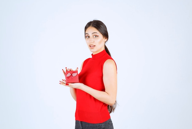 Ragazza in camicia rossa che dimostra la sua confezione regalo rossa.