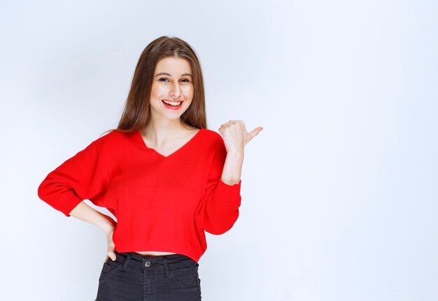 Ragazza in camicia rossa che indica qualcosa dietro.