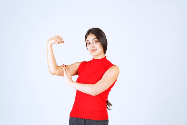 Ragazza in camicia rossa che mostra i suoi muscoli e pugni del braccio.