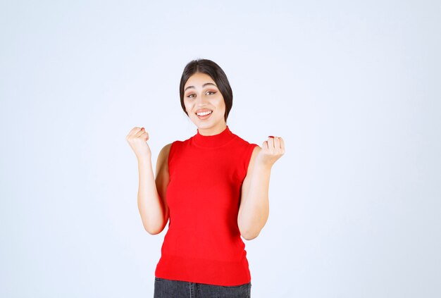 Ragazza in camicia rossa che mostra i suoi muscoli e pugni del braccio.