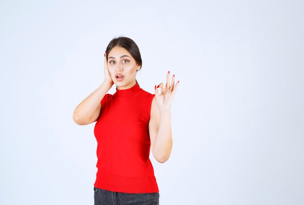 Ragazza in camicia rossa che mostra il segno positivo della mano.