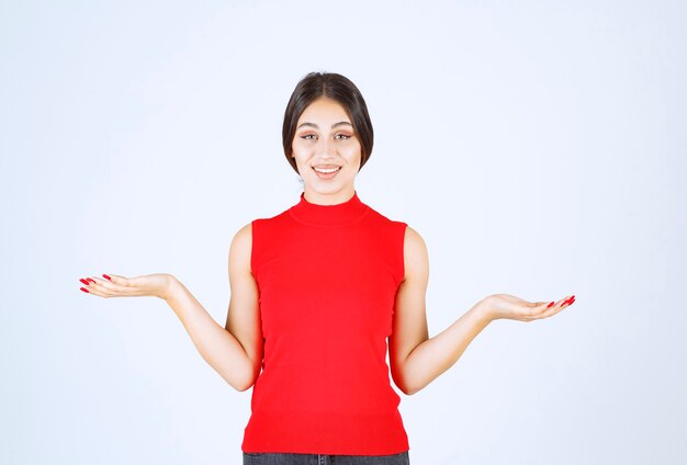 Ragazza in camicia rossa che mostra qualcosa nella sua mano aperta.