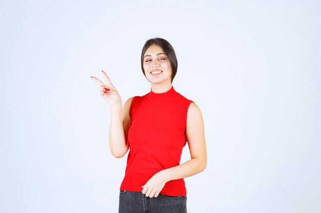 Ragazza in camicia rossa che mostra segno di pace e amicizia.