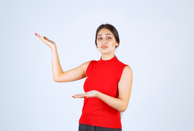 Ragazza in camicia rossa che presenta e mostra qualcosa in mano.