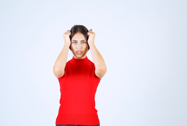 Ragazza in camicia rossa che si tiene la testa con le mani perché ha mal di testa.