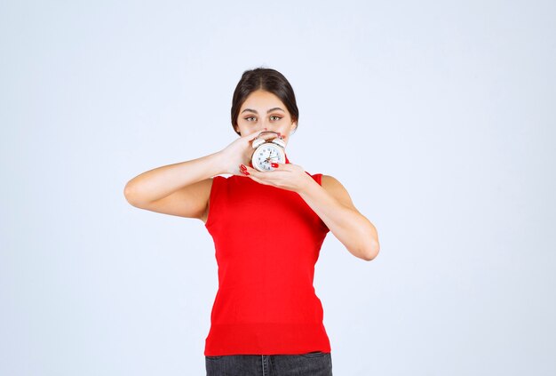 Ragazza in camicia rossa che tiene e promuove una sveglia.