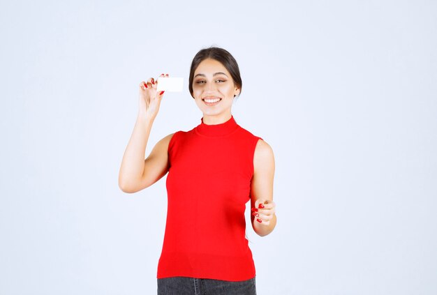 Ragazza in camicia rossa che tiene un biglietto da visita e sembra soddisfatta.