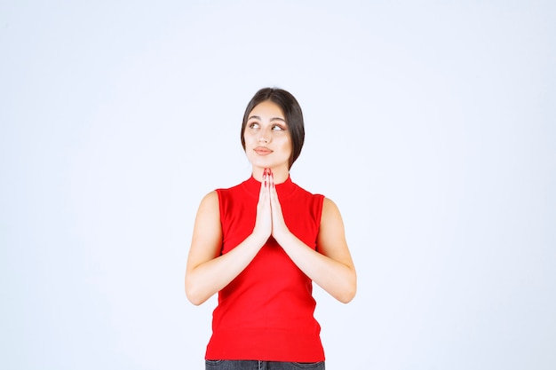 Ragazza in camicia rossa che unisce le mani e prega.