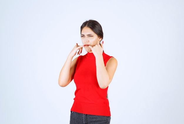 Ragazza in camicia rossa mettendo le mani in bocca e fischiettando.