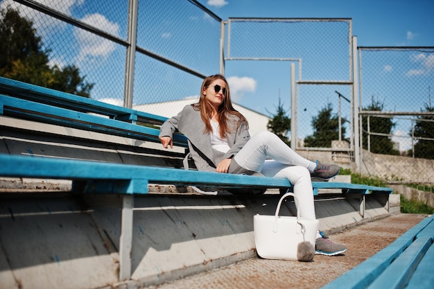 Ragazza in cappotto grigio con occhiali da sole al piccolo stadio di strada