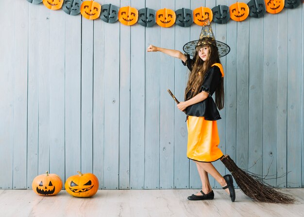 Ragazza in costume da strega in piedi con la scopa