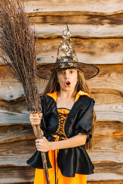 Ragazza in costume della strega che fa fronte con il manico di scopa