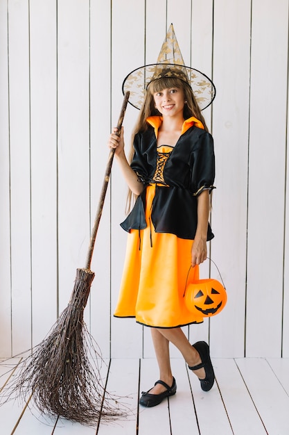 Ragazza in costume di Halloween con cesto e scopa in posa in studio