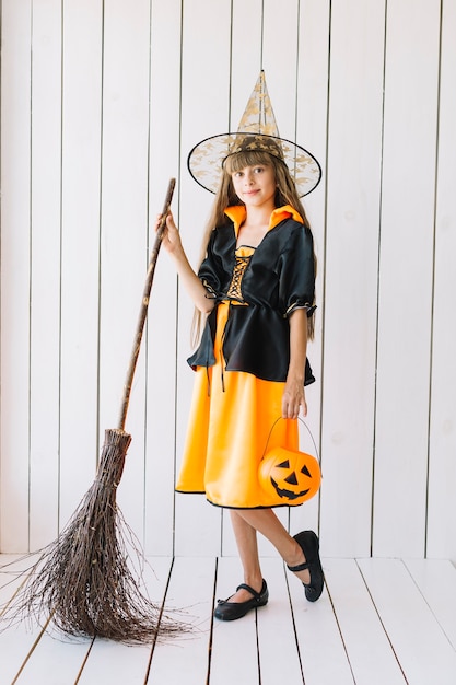 Ragazza in costume di Halloween con scopa in posa in studio