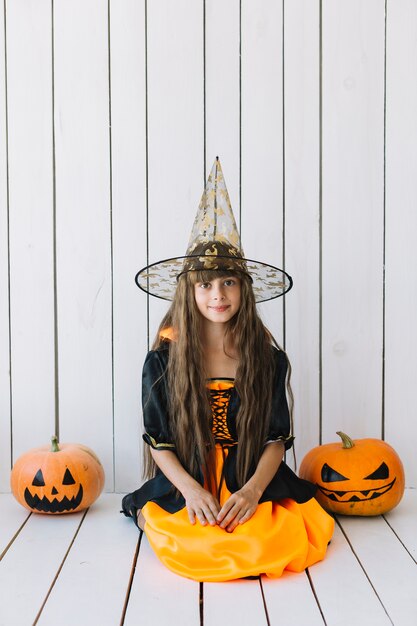 Ragazza in costume di Halloween con zucche sui lati seduto in studio