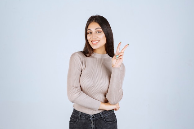 Ragazza in maglione grigio che fa il segno della mano di pace.