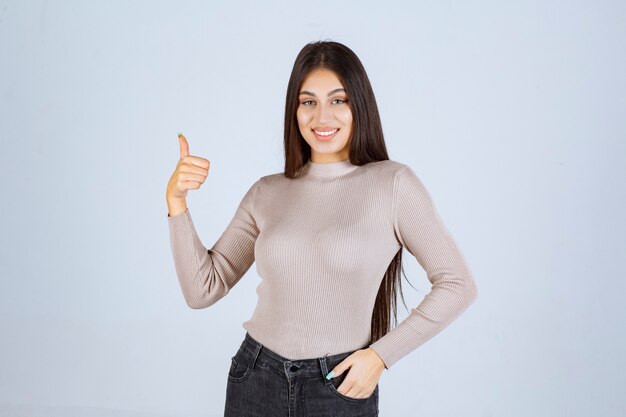 Ragazza in maglione grigio che fa pollice sul segno.