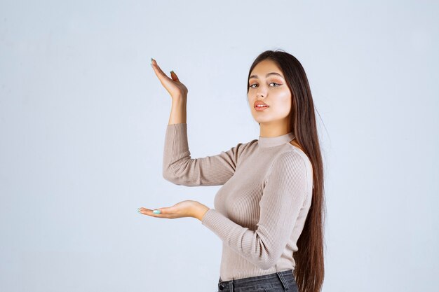 Ragazza in maglione grigio che mostra qualcosa a sinistra.