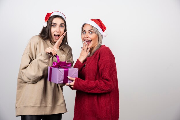 Ragazza in maglione rosso che fa un regalo alla ragazza in maglione beige.