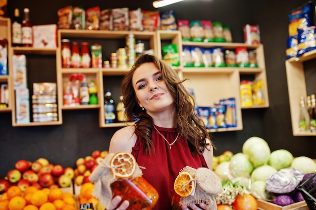 Ragazza in marmellata rossa della holding in un barattolo sul negozio di frutta