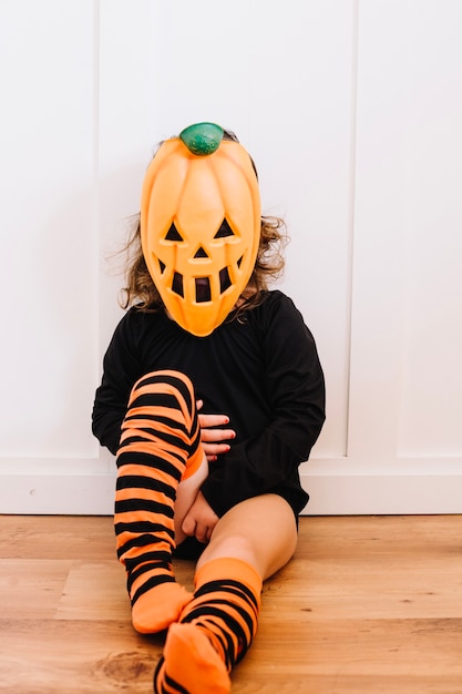 Ragazza in maschera jack-o-lanterna seduta sul pavimento