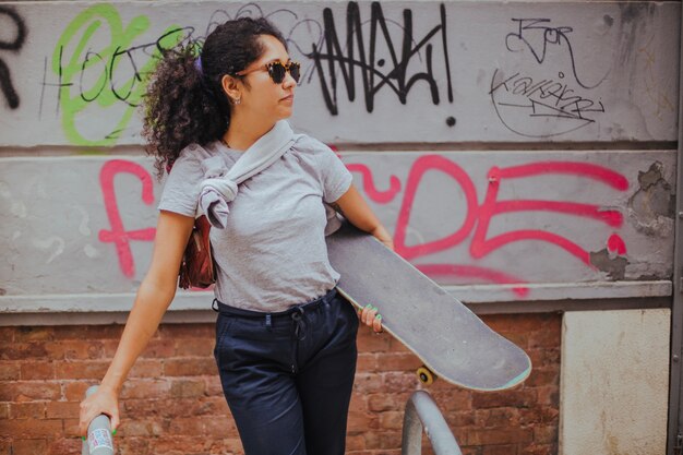 Ragazza in piedi fuori che tiene skateboard pendente