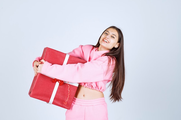 Ragazza in pigiama rosa che abbraccia una grande confezione regalo rossa e sorridente.