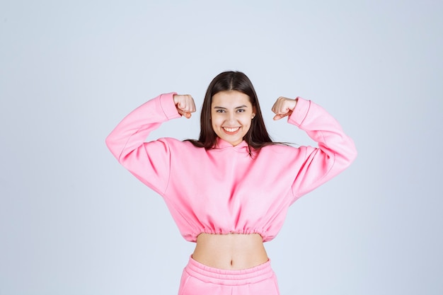 Ragazza in pigiama rosa che mostra i suoi muscoli del braccio