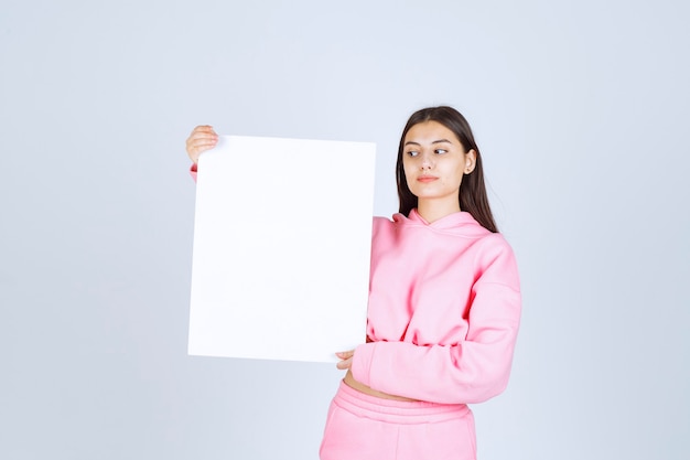 Ragazza in pigiama rosa che tiene una scheda di presentazione quadrata vuota di un nuovo progetto.