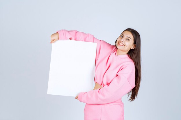 Ragazza in pigiama rosa che tiene una scheda di presentazione quadrata vuota di un nuovo progetto.