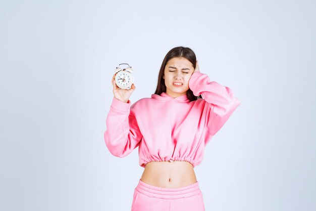 Ragazza in pigiama rosa che tiene una sveglia e viene disturbata a causa del rumore.